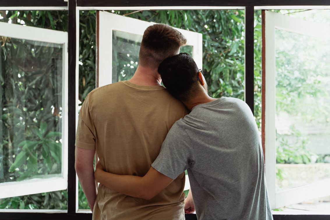 Una pareja abrazada mira por la ventana de su casa